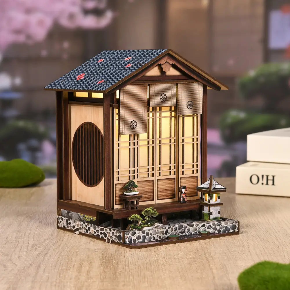 A miniature wooden japanese style moss lantern harmony house with dark blue roof and led light glowing from within australia